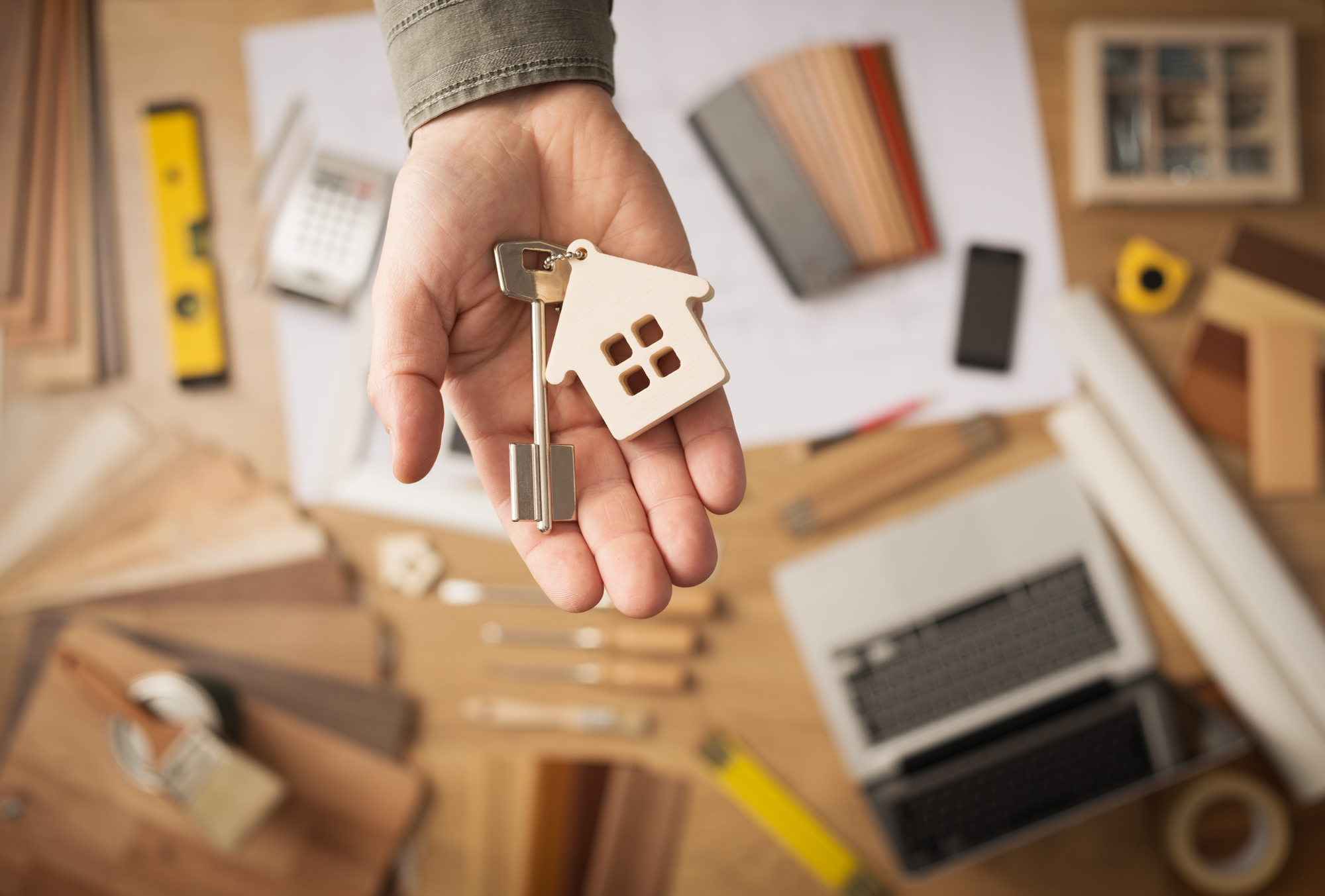 A person holds a house key in one hand and a small model of a house in the other, symbolizing home ownership.