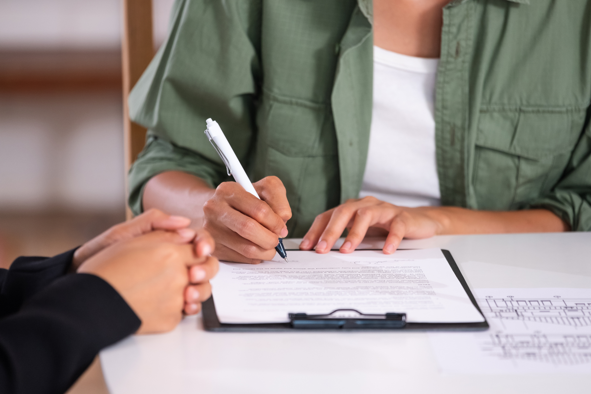 A woman signs a contract while two other individuals observe and discuss the agreement beside her