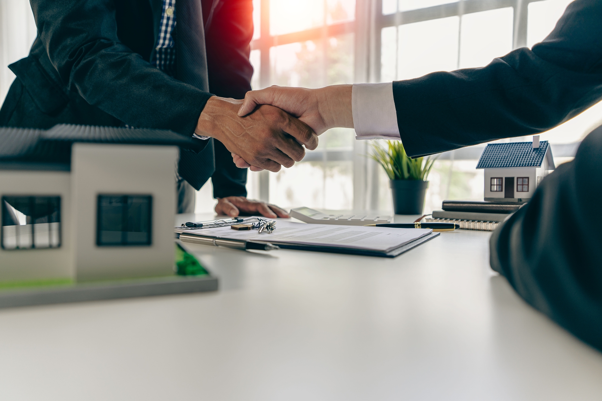 Two businessmen shake hands over a table featuring a model house